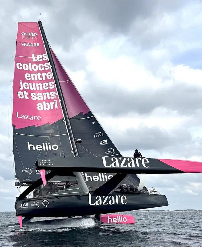 LAZARE sous voiles, grand-voile rose et noire, le trimaran soulevé au-dessus de l'eau